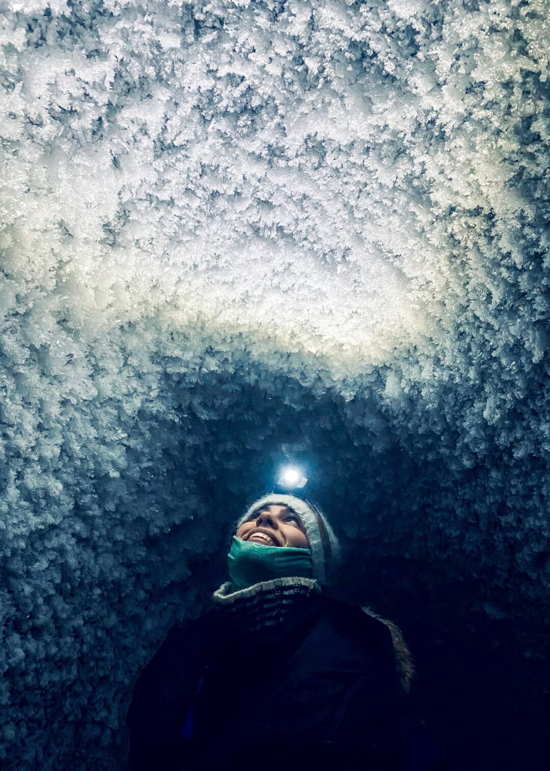 Woman in winter clothing smiling in falling snow at night, outdoors.