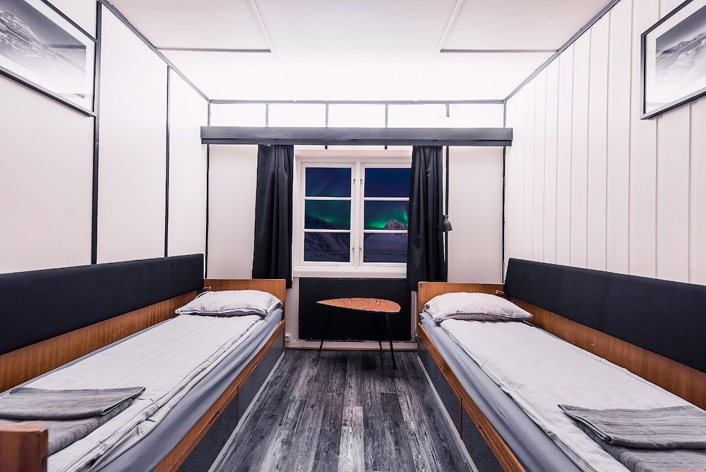 Two single beds in a shared adventure lodge cabin with curtains, window view and wooden interior walls