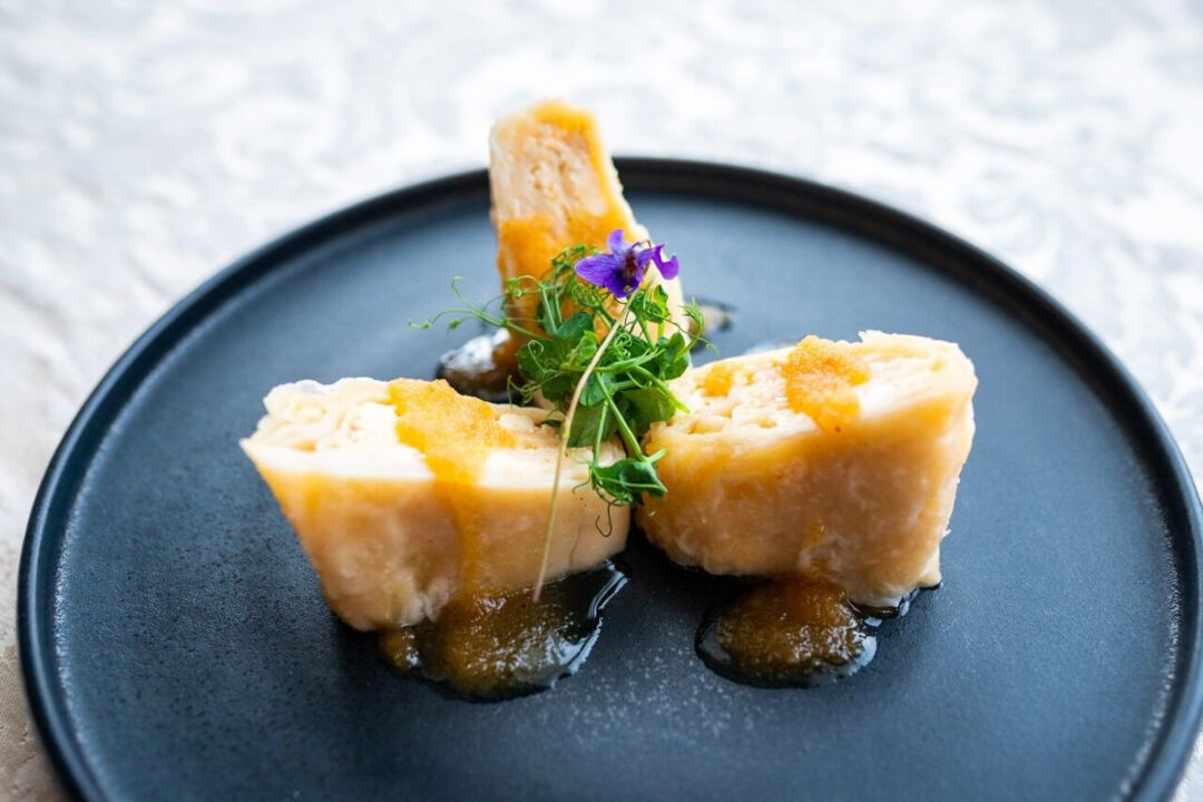 Garnished dish on a dark plate with butter cubes and purple edible flowers