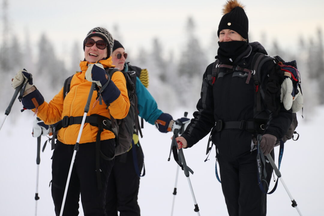 Women backcountry ski trek in snowy forest, smiling skier with skis and poles at winter camp.
