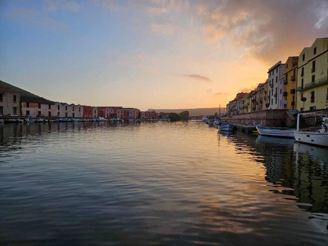 Harbour at sunset with moored boats and waterfront buildings along a calm canal