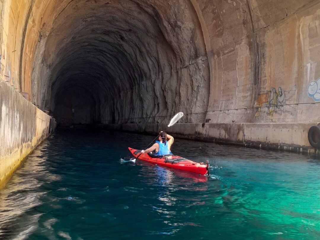 Woman paddling a kayak through a submerged tunnel pool, with clear blue water indoors