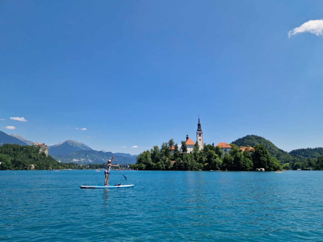 Woman paddleboarding on a calm lake with a church island in the background.