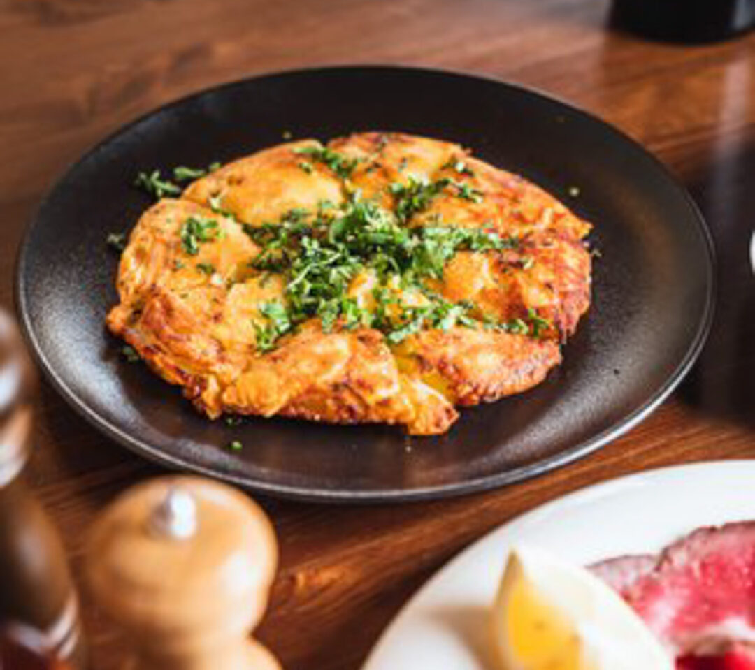 Savoury chicken cutlets topped with chopped herbs on a black plate on a wooden table