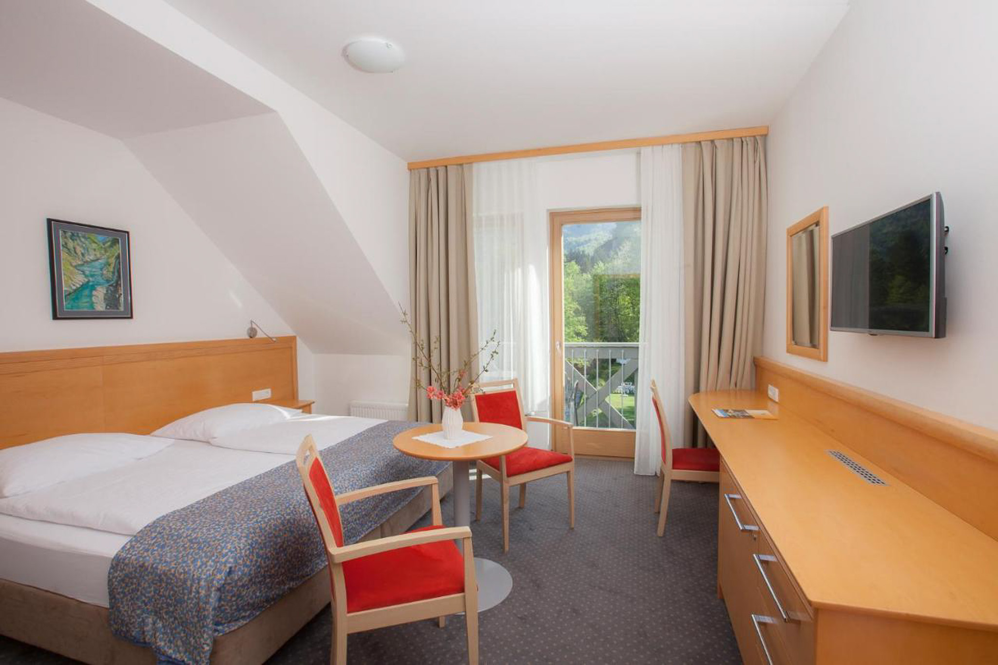 Hotel bedroom with double bed, desk, TV and dining table by a window, featuring a mountain view outdoors
