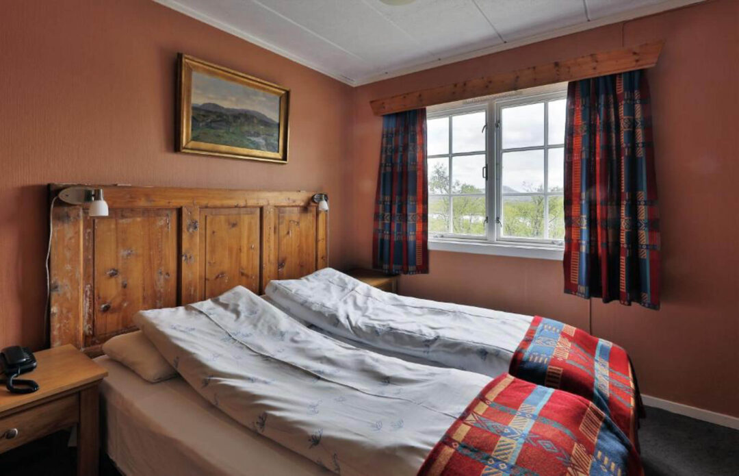 Cozy bedroom with a double bed, wooden headboard, and large window with patterned curtains