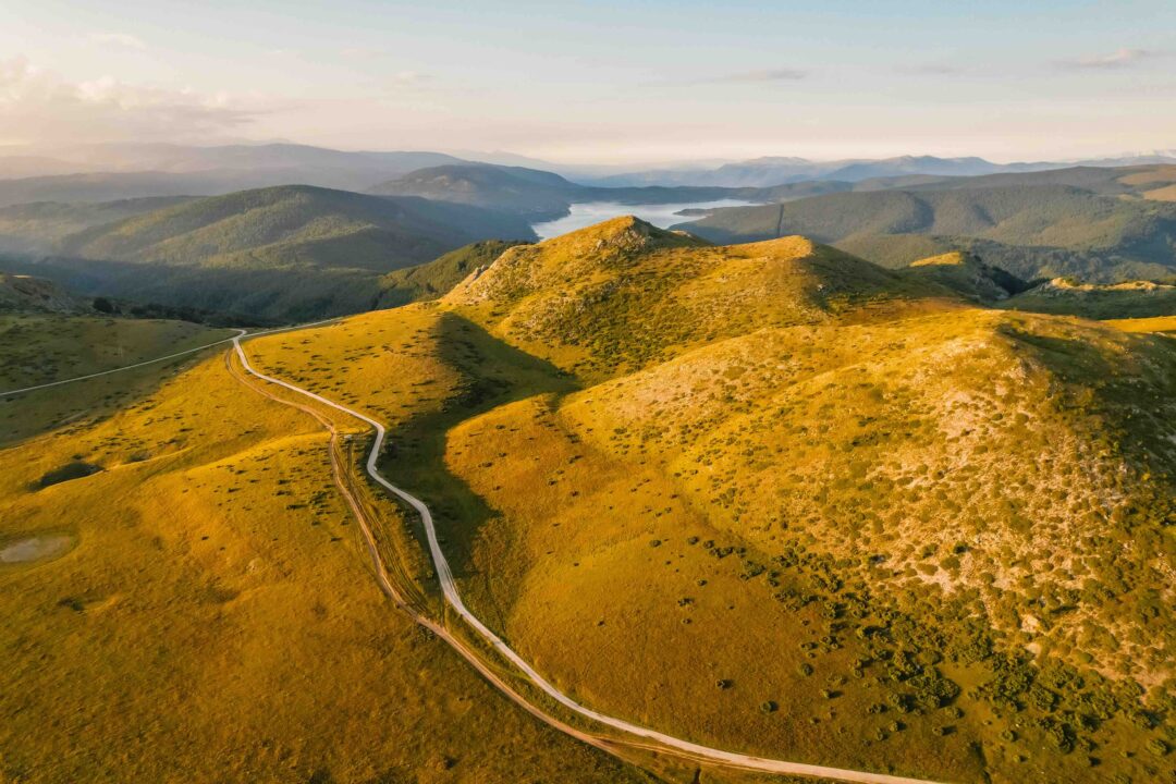 Winding road through rolling mountain hills at golden hour, scenic valley landscape
