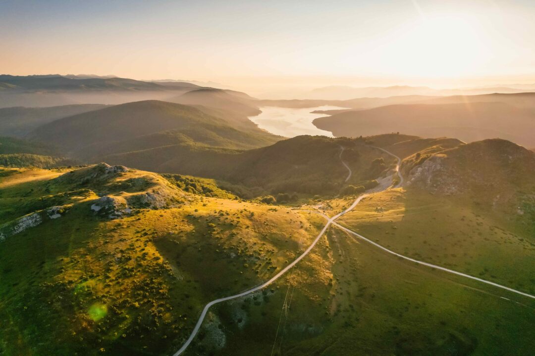 Aerial view of a mountain valley in North Macedonia at sunrise, with a winding road through green hills and river.