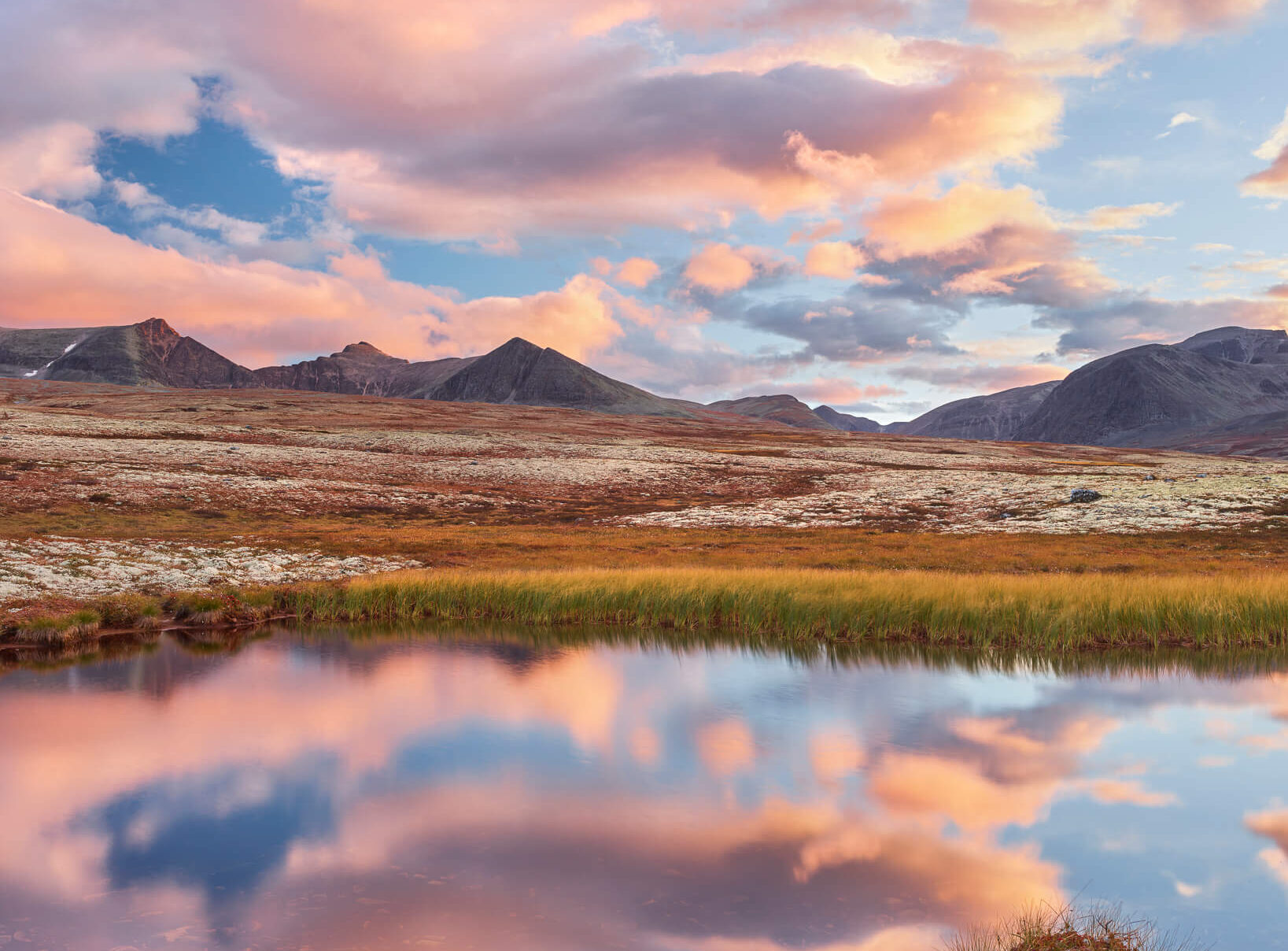 Mountain landscape with calm lake reflection at sunset, wide valley and rocky peaks in Norway