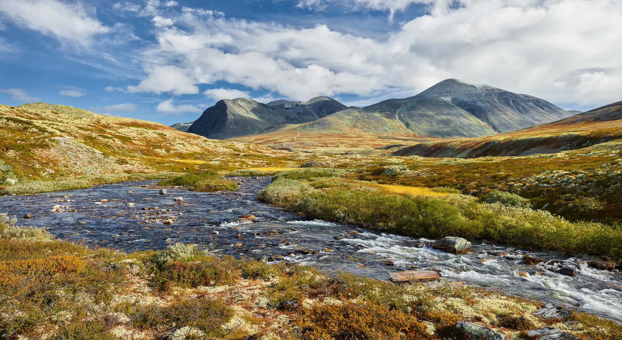 Mountain river winding through a Norwegian valley landscape with hills and peaks under a cloudy sky