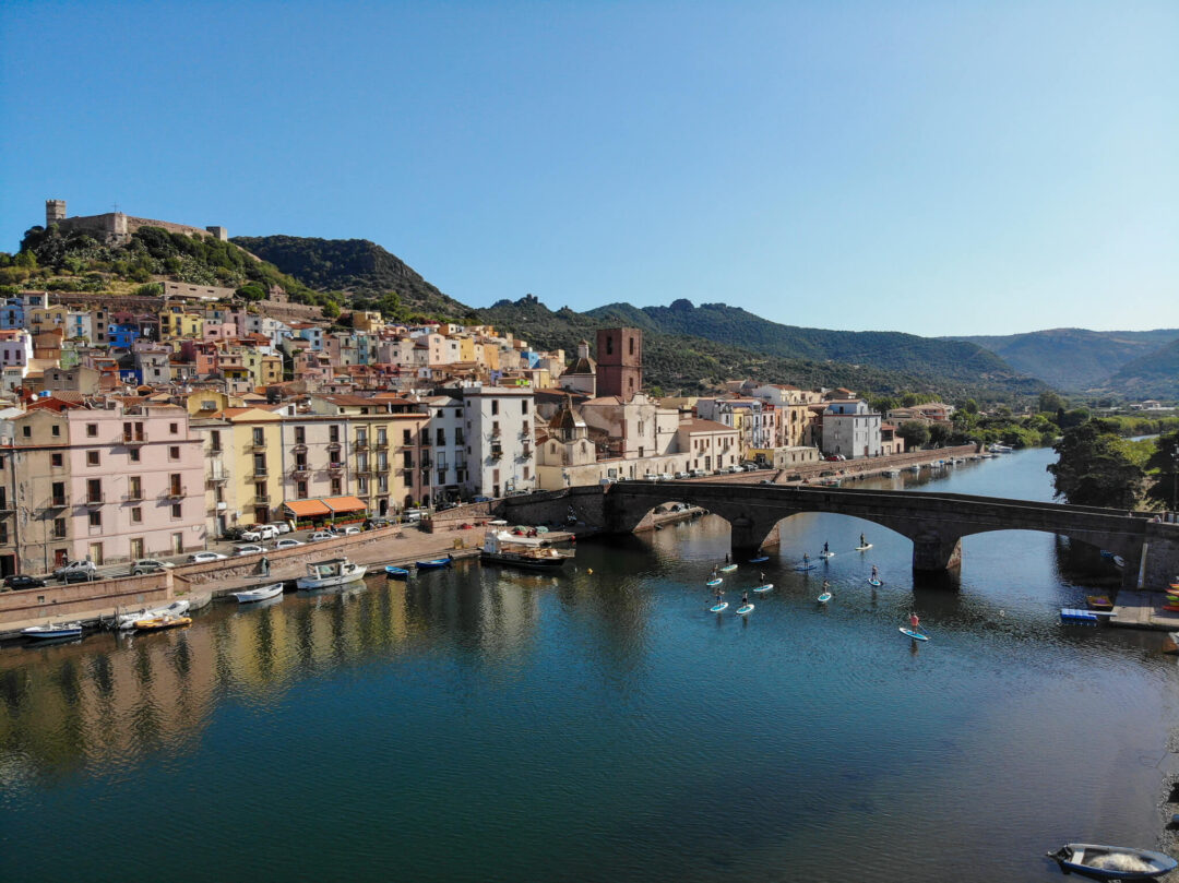 Coastal Italian town harbour with arched bridge and moored boats under a blue sky