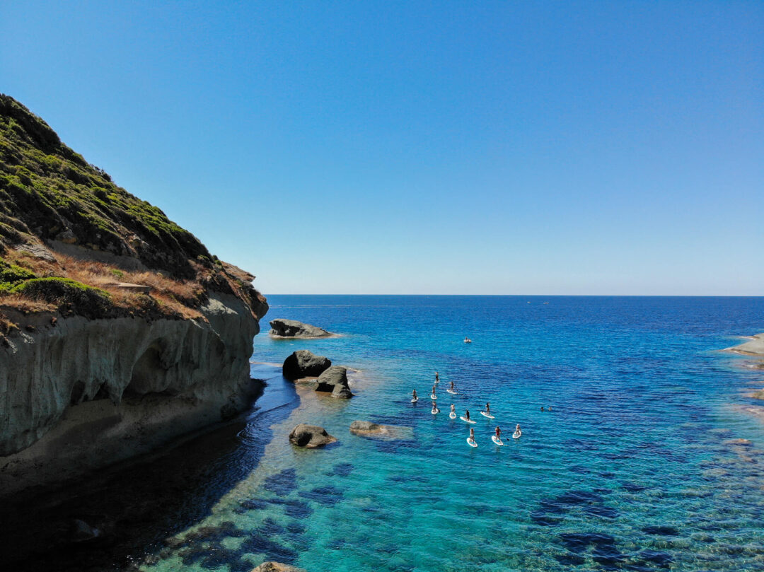 Stand-up paddleboarders in clear turquoise sea near a rocky coastline