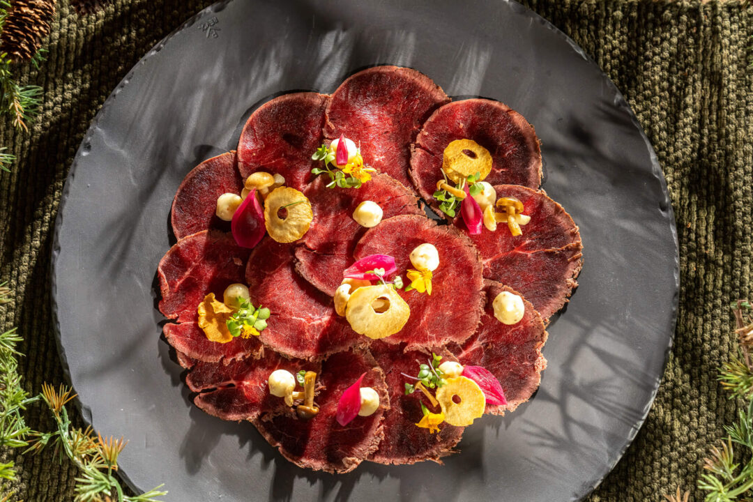 Red meat platter with colourful vegetable and herb garnishes on a dark tray, ready to serve