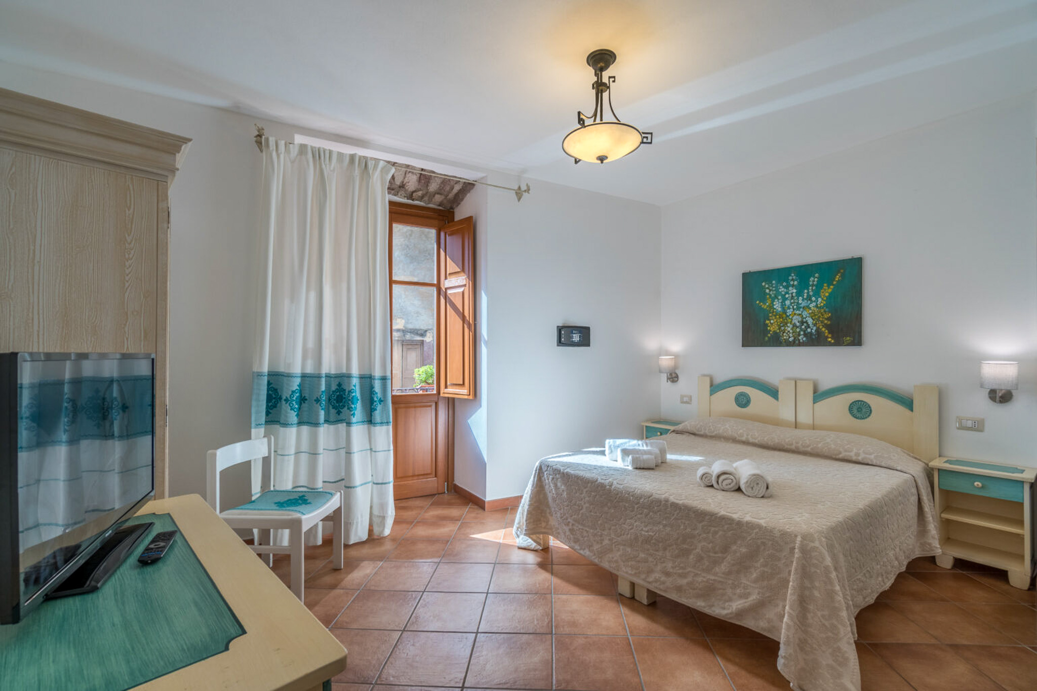 Bright hotel bedroom with double bed, tiled floor, curtains and window—Sardinia accommodation interior