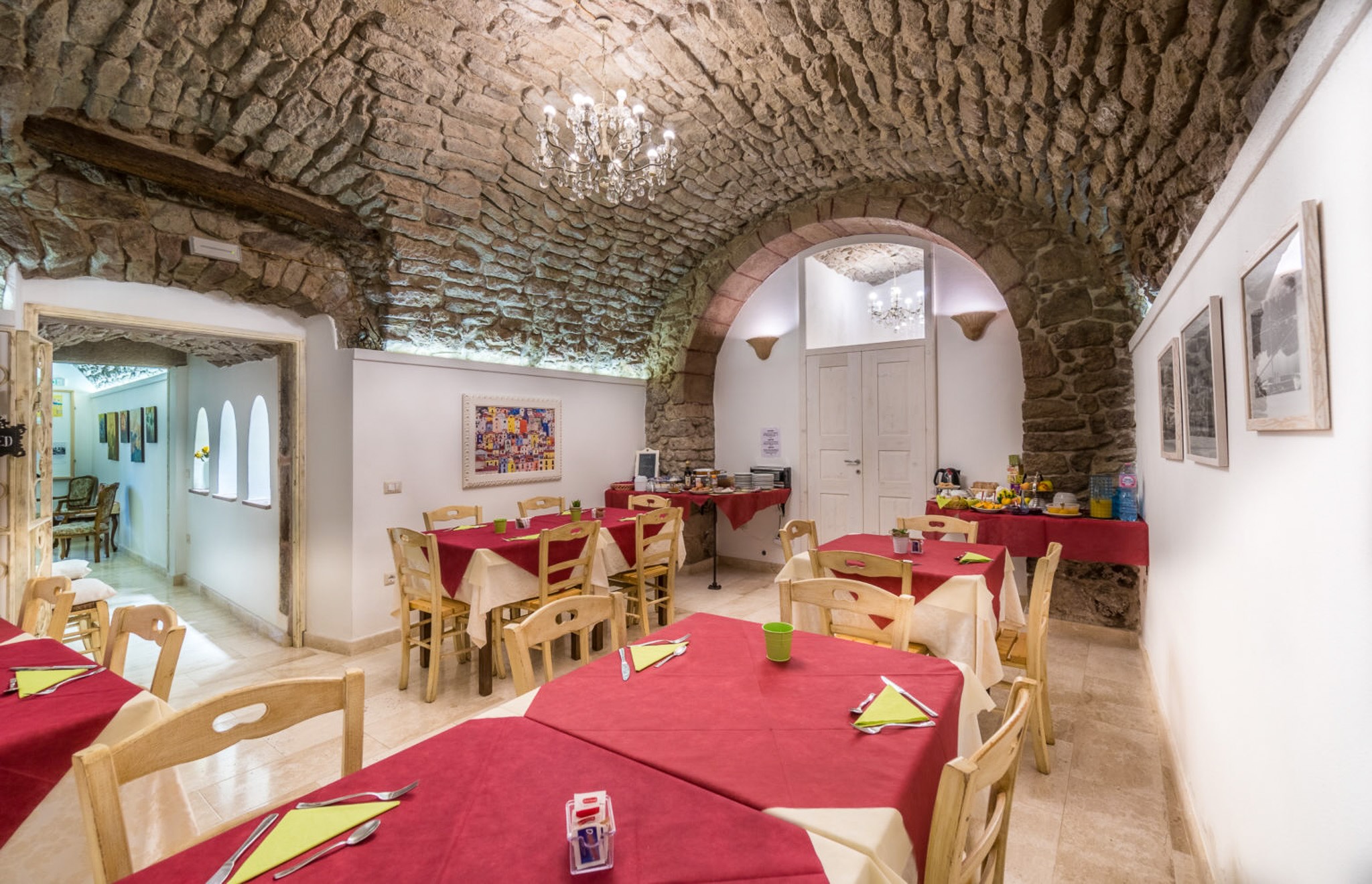 Stone-vaulted dining room with set tables and red tablecloths for a supper in Sardinia