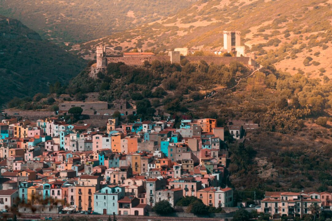 Sardinian hillside town with colourful houses and a distant historic church among olive groves