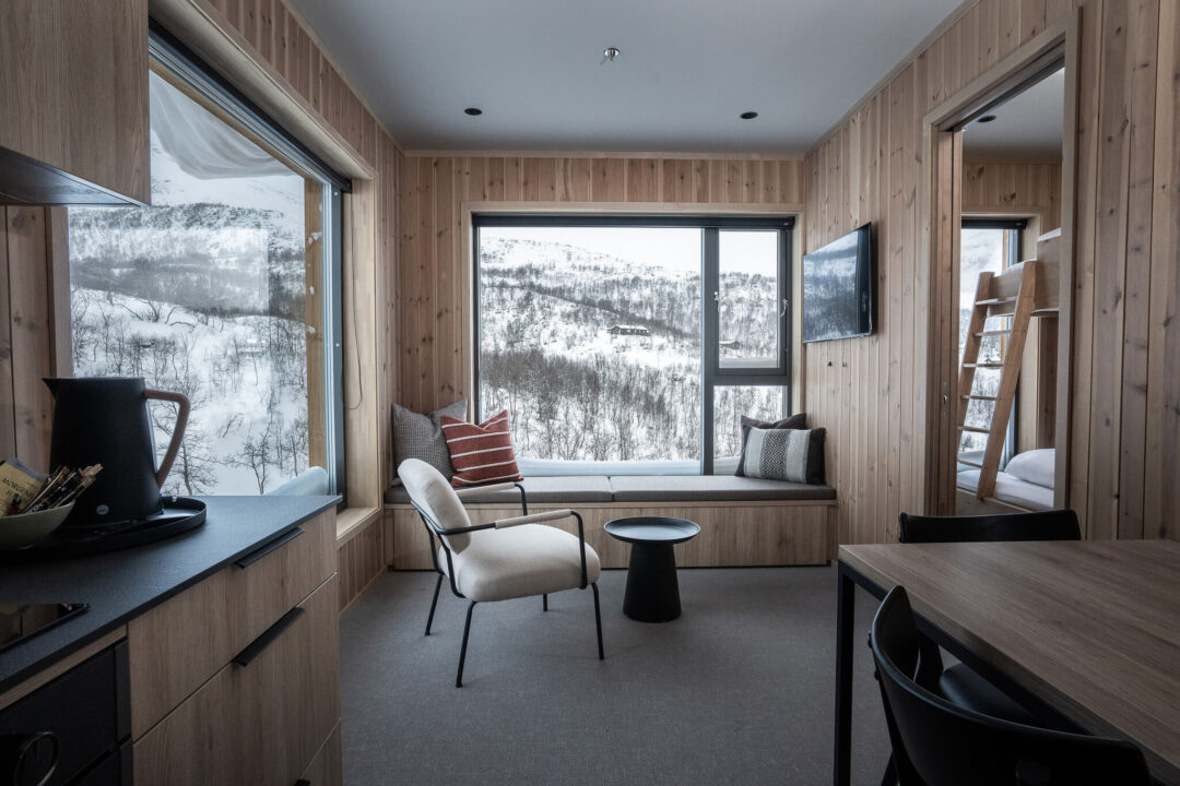 Cozy Norwegian cabin lounge with large windows overlooking a snowy mountain landscape