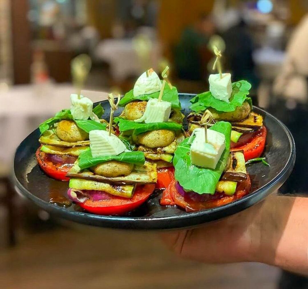 Vegetarian appetiser plate of grilled aubergine and peppers topped with fresh herbs and feta cheese.