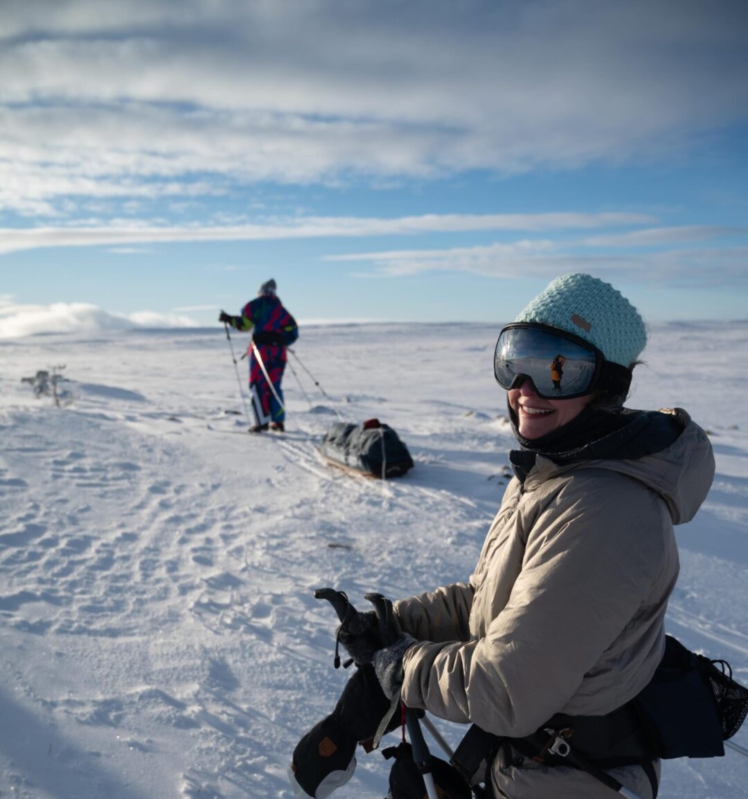Woman in ski goggles and winter clothing skis through snowy backcountry terrain on a winter expedition