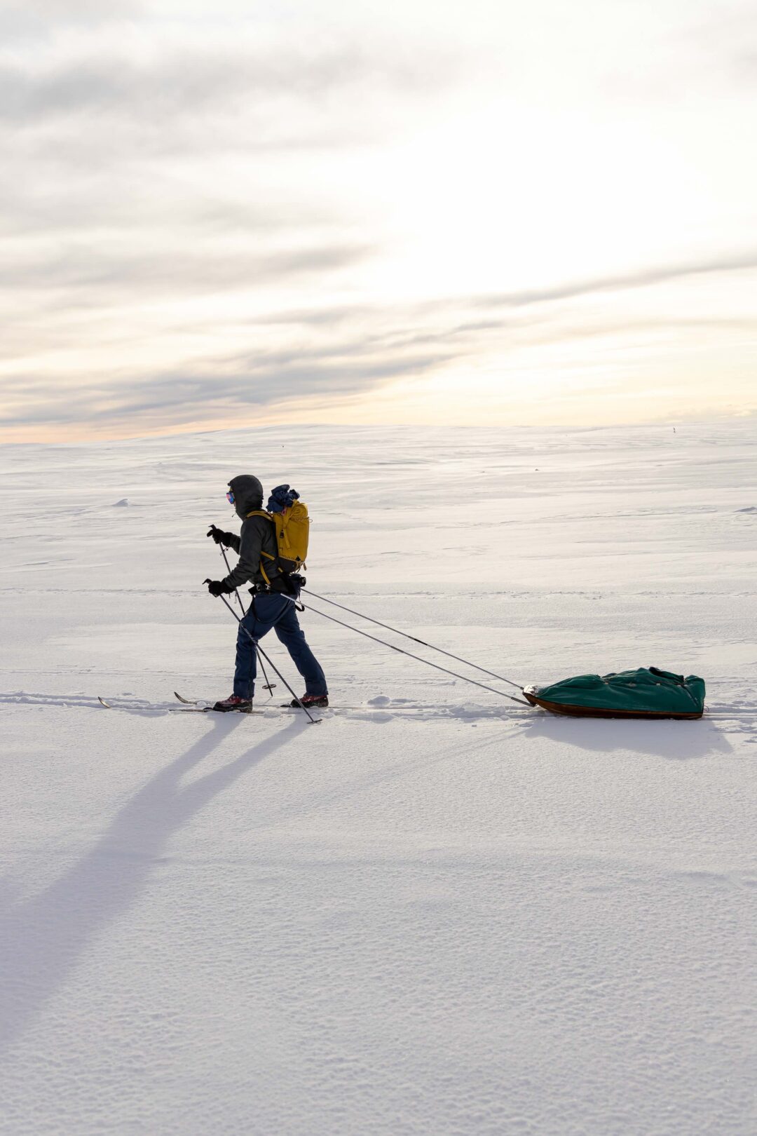 Woman ski-touring across snowy wilderness with winter camping gear and a sled