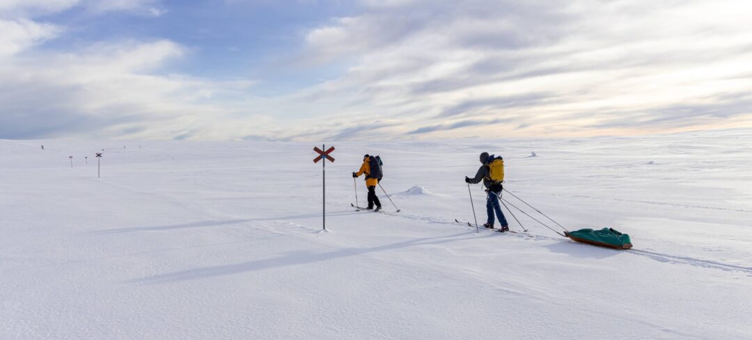 Women backcountry skiing in Sweden on a snowy winter trail with skis and a sledge in the distance
