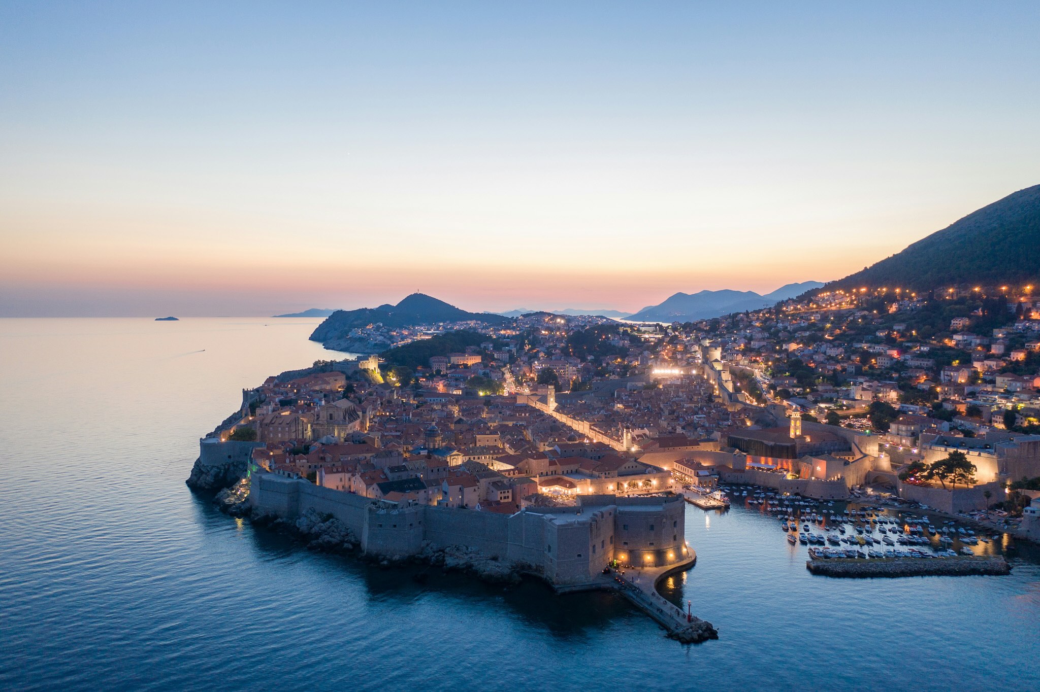 Coastal town at dusk with harbour lights, aerial view over the shoreline and sea