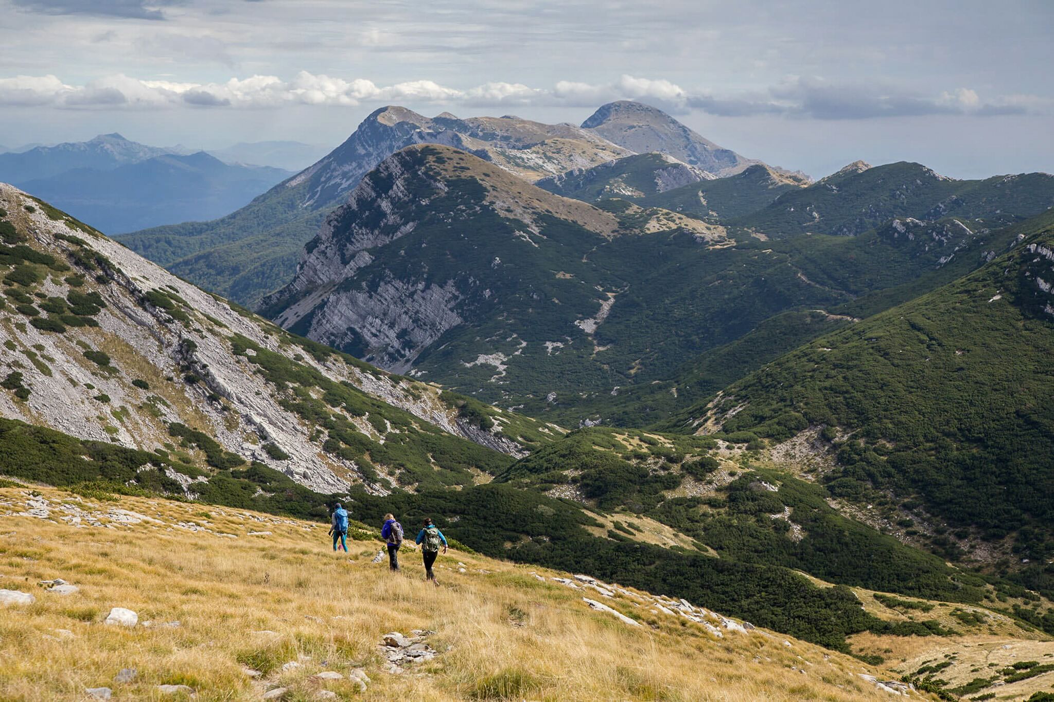 Women hiking with backpacks on a mountain trail over the Alps landscape in Europe