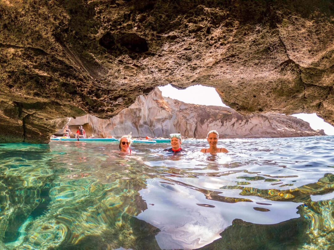 Women on stand-up paddle boards in clear sea near a rocky cove, Sardinia.