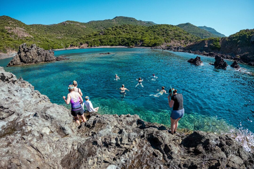 Women stand on rocks and swim in clear turquoise sea near the Sardinia coast, summer adventure.