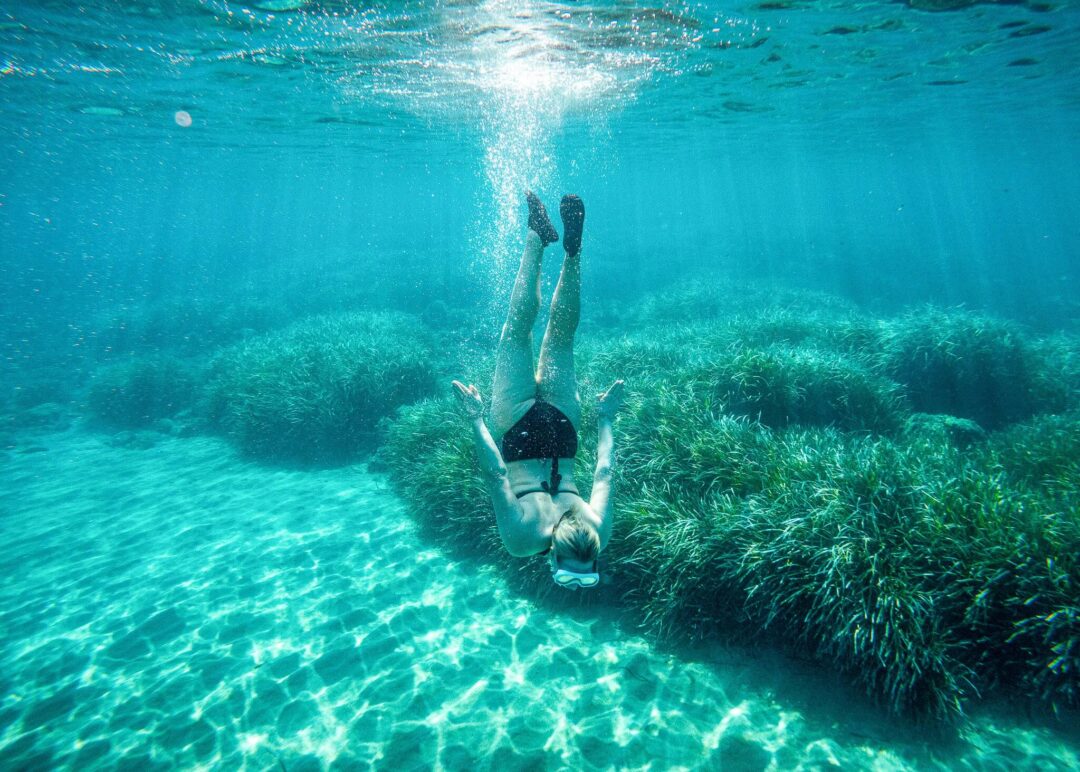 Woman swimming underwater in clear sea near seagrass, snorkelling-style adventure holiday