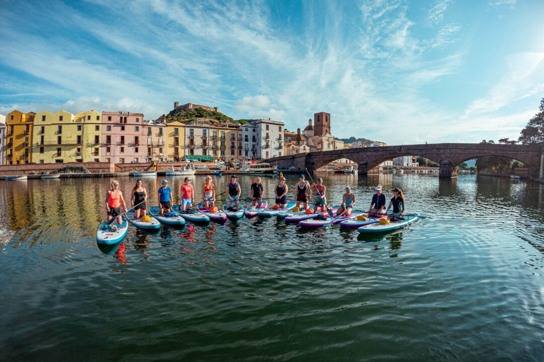 Women on stand-up paddleboards in Sardinia, group SUP lesson on a river with a bridge and town in view