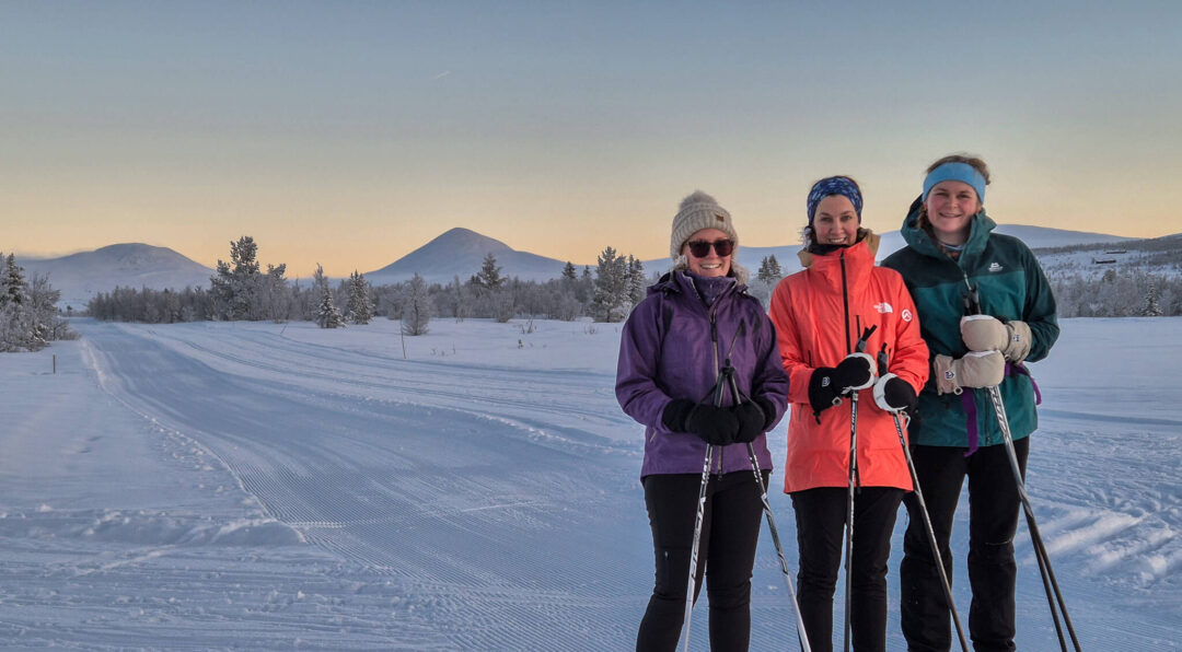 Women cross-country skiing on snowy tracks in Norway at sunrise