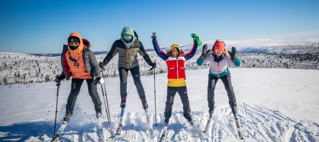 Women ski on a snow-covered trail in a winter landscape, posing with poles and skis on a clear day