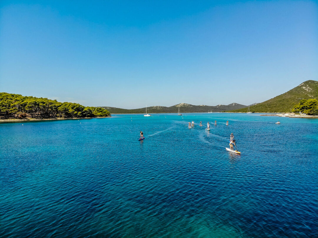 Women paddleboarding in a calm, clear blue sea in a coastal bay