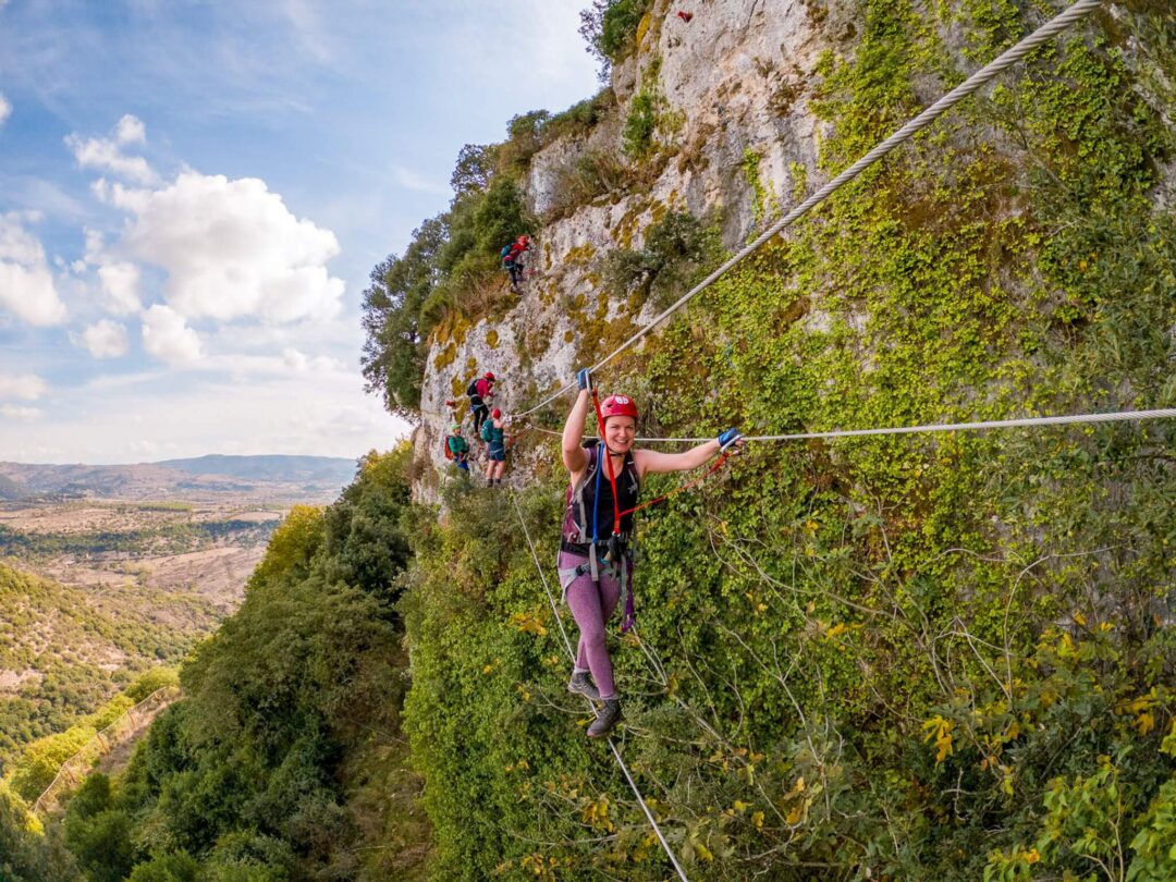 Women hiking on a cliff via a rope line in Sardinia landscape, outdoors adventure.