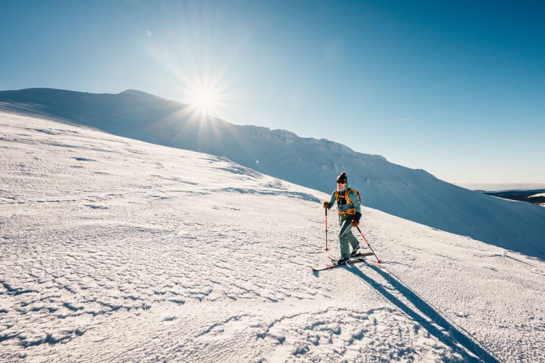 Woman trekking on a snowy mountain ridge in bright sunshine