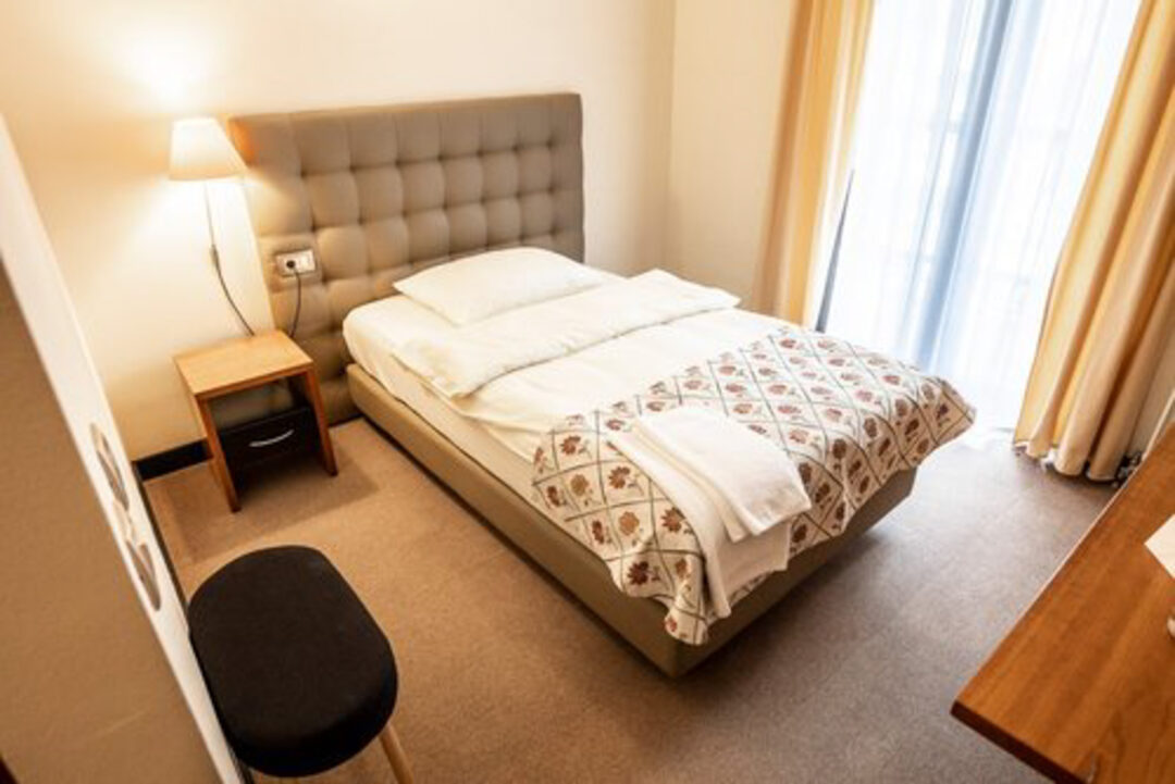 Unmade double bed in a bright hotel room with bedside lamp and curtains