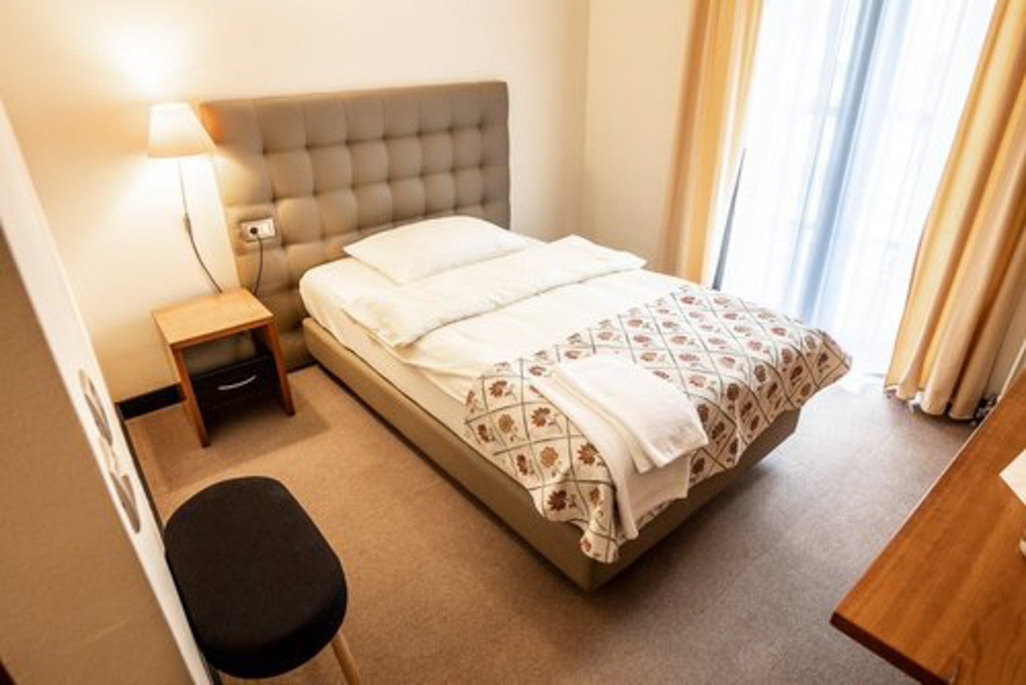 Unmade double bed in a bright hotel room with bedside lamp and curtains