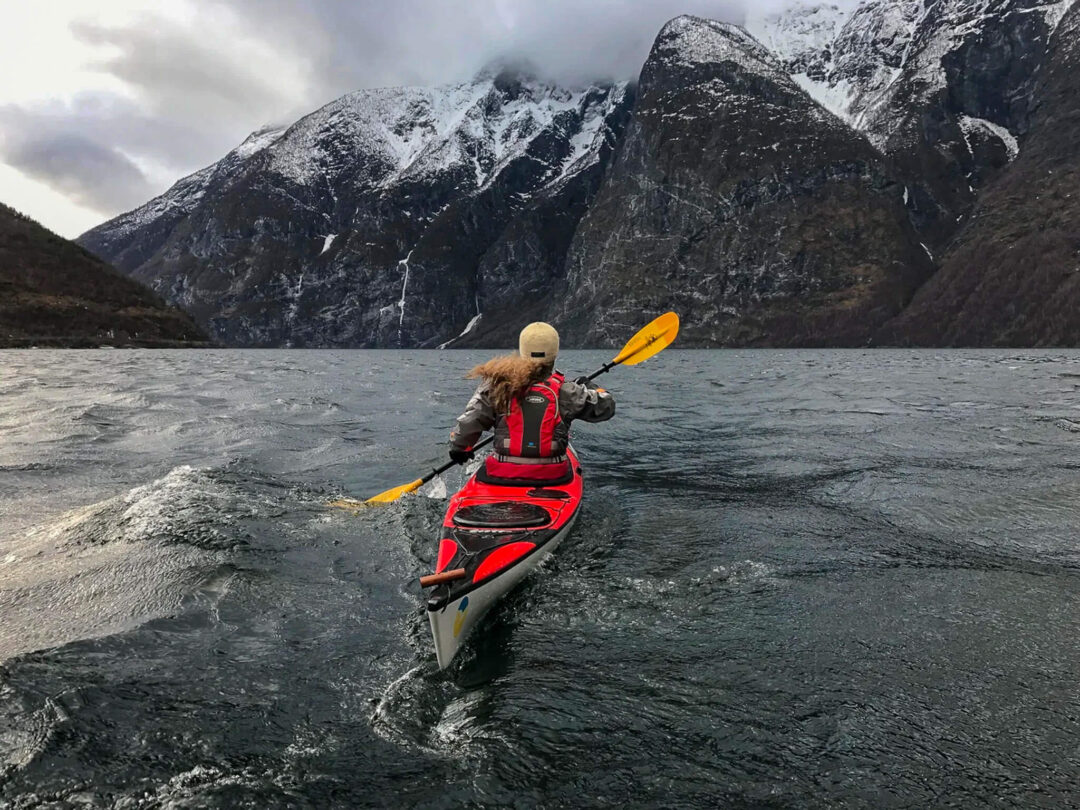 Woman paddling a kayak on an icy fjord with snow-covered mountains in the background