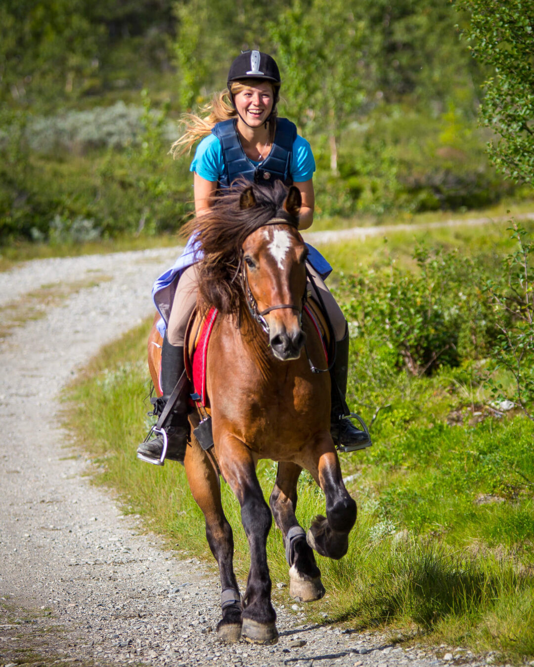 Woman horse riding along a gravel trail in green countryside