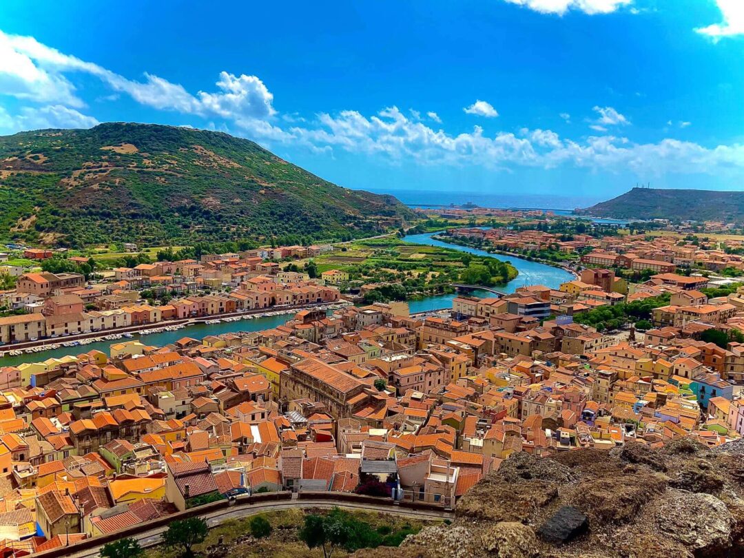 Aerial view of a Mediterranean hillside town in Sardinia with river and sea under a clear blue sky