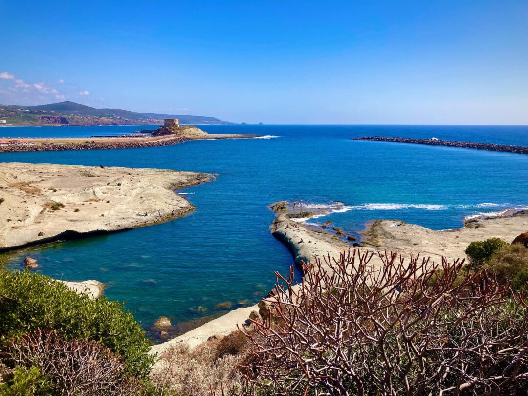 Coastal scenery in Sardinia, turquoise sea with rocky shoreline and breakwater in calm blue water