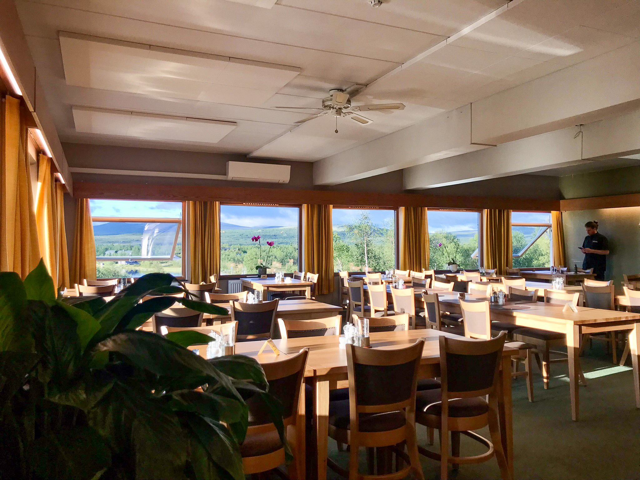 Empty dining room with set tables and large windows overlooking a green valley