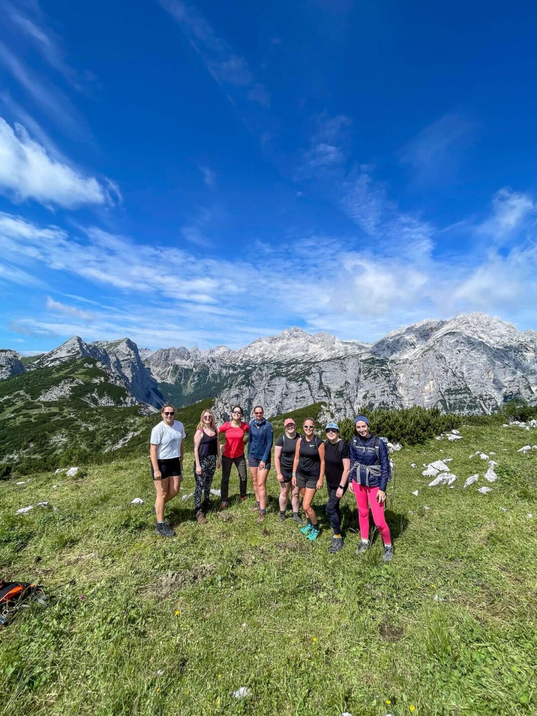Women hiking on a grassy trail with Alpine mountains in Slovenia under a blue sky