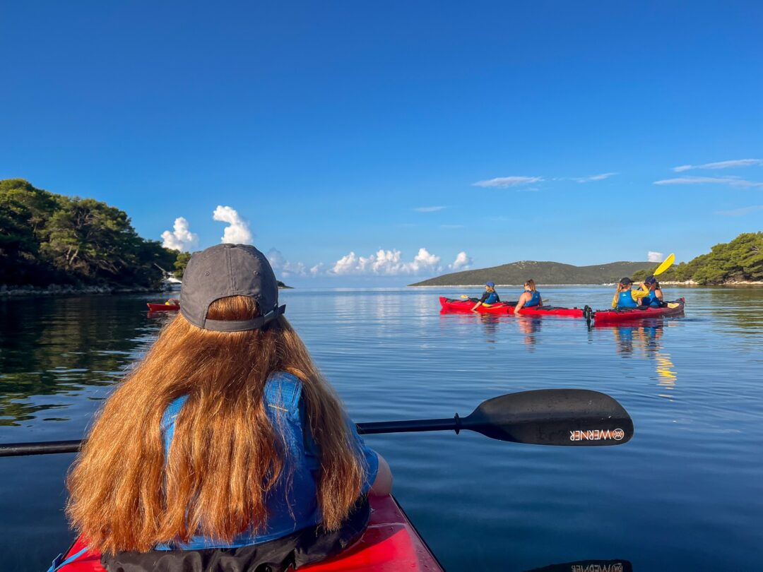 Women paddling kayaks on calm water at a coastal inlet under a blue sky