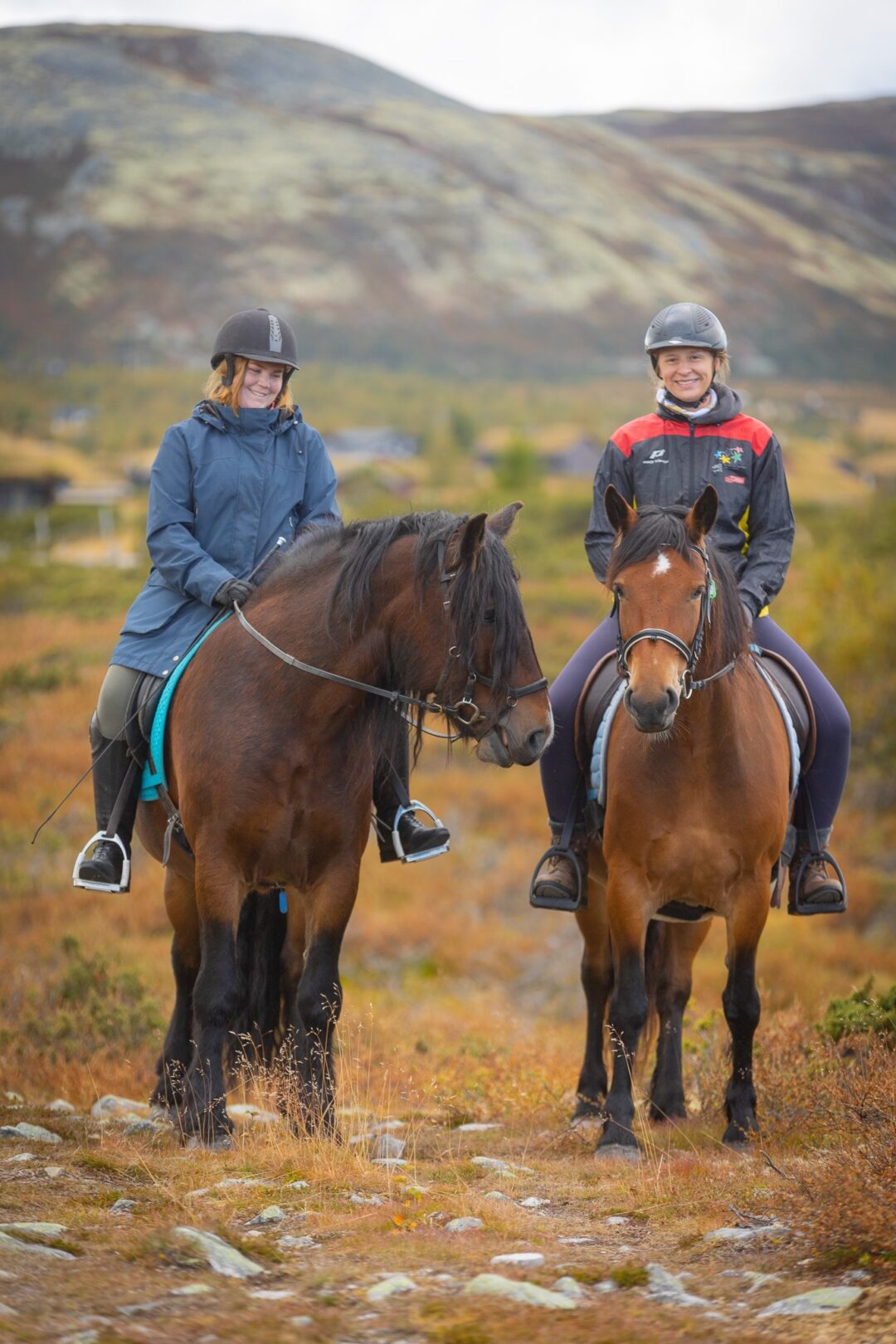 Two women on horseback, smiling at a mounted start on a rocky mountain trail