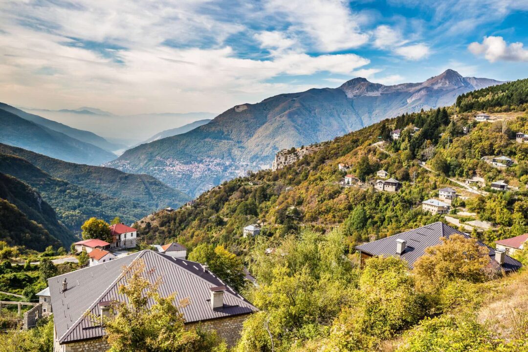 Mountain valley landscape with forested slopes and village houses under a blue sky