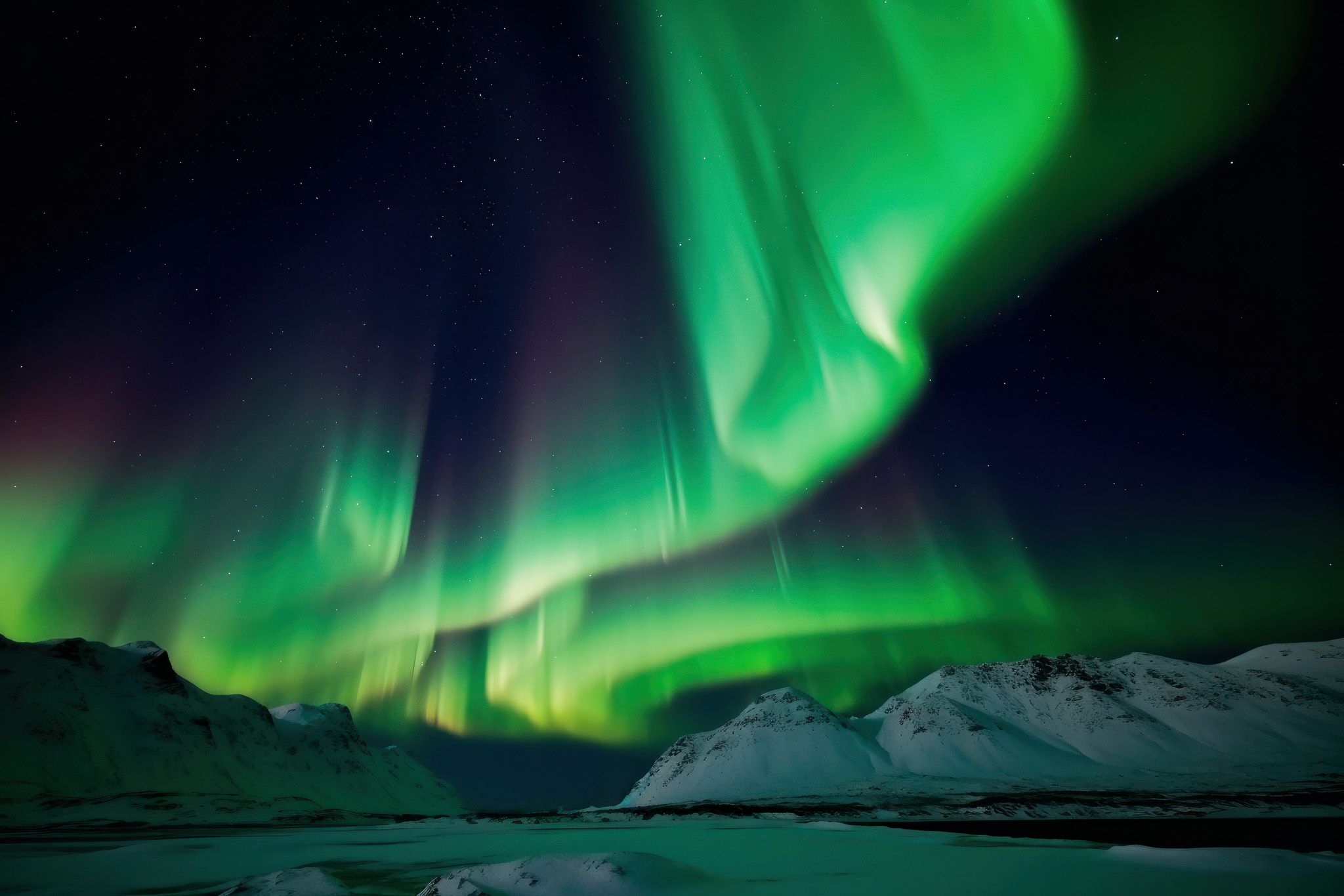 Northern lights aurora over snowy mountains and a frozen landscape at night in the Arctic