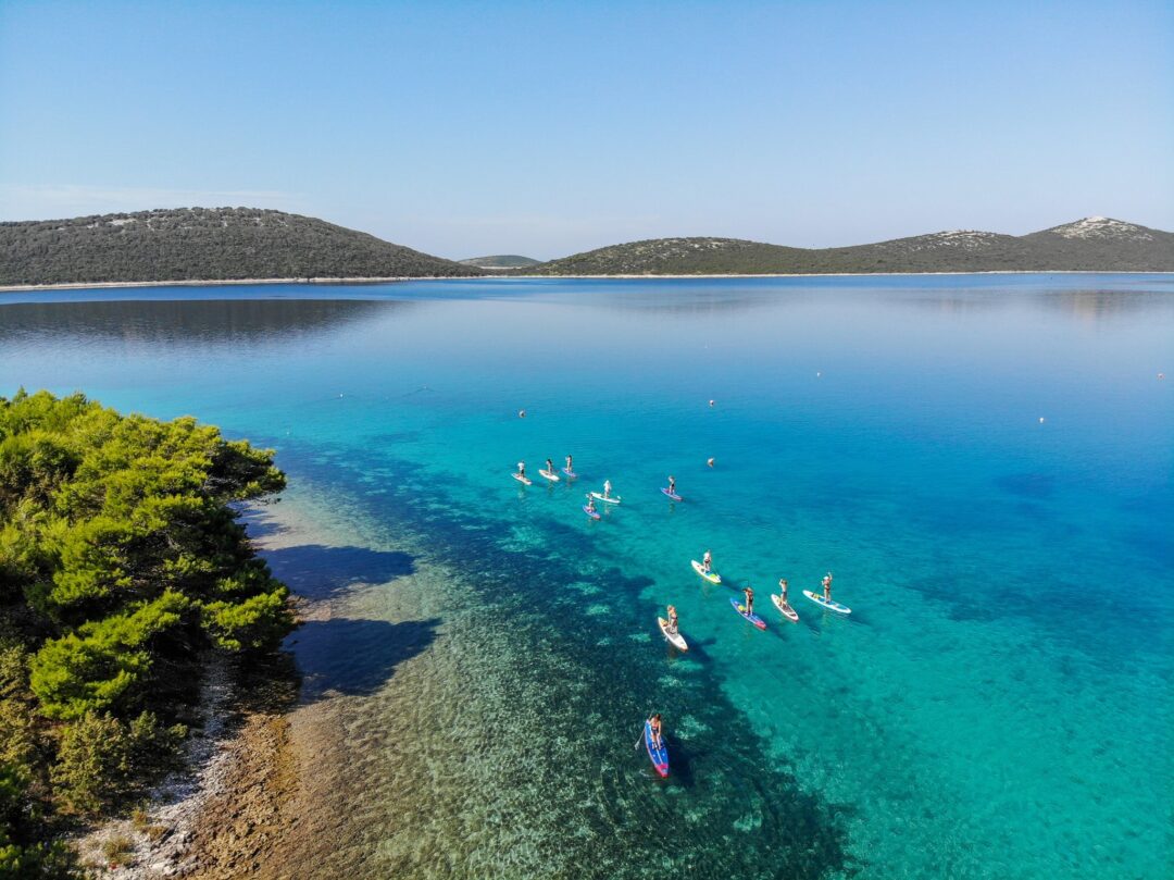 Kayakers on turquoise water in a coastal cove with low islands and clear blue sky