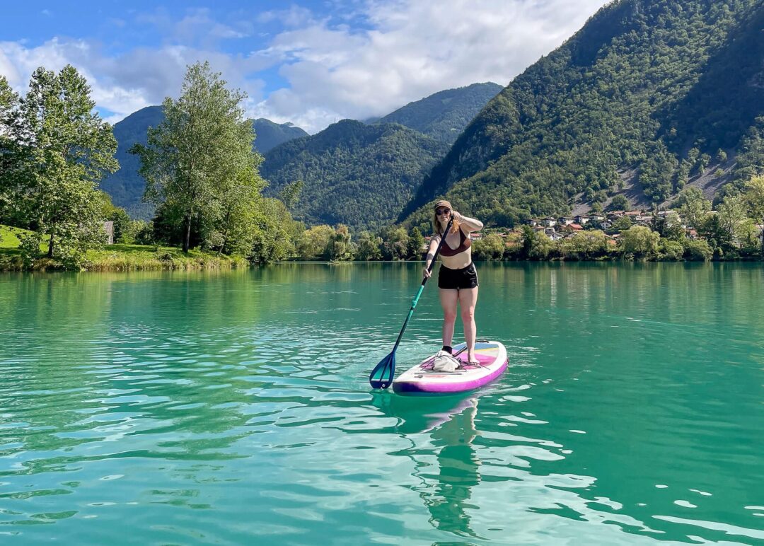 Woman paddleboarding on a mountain lake with forested hills and riverside homes in the background